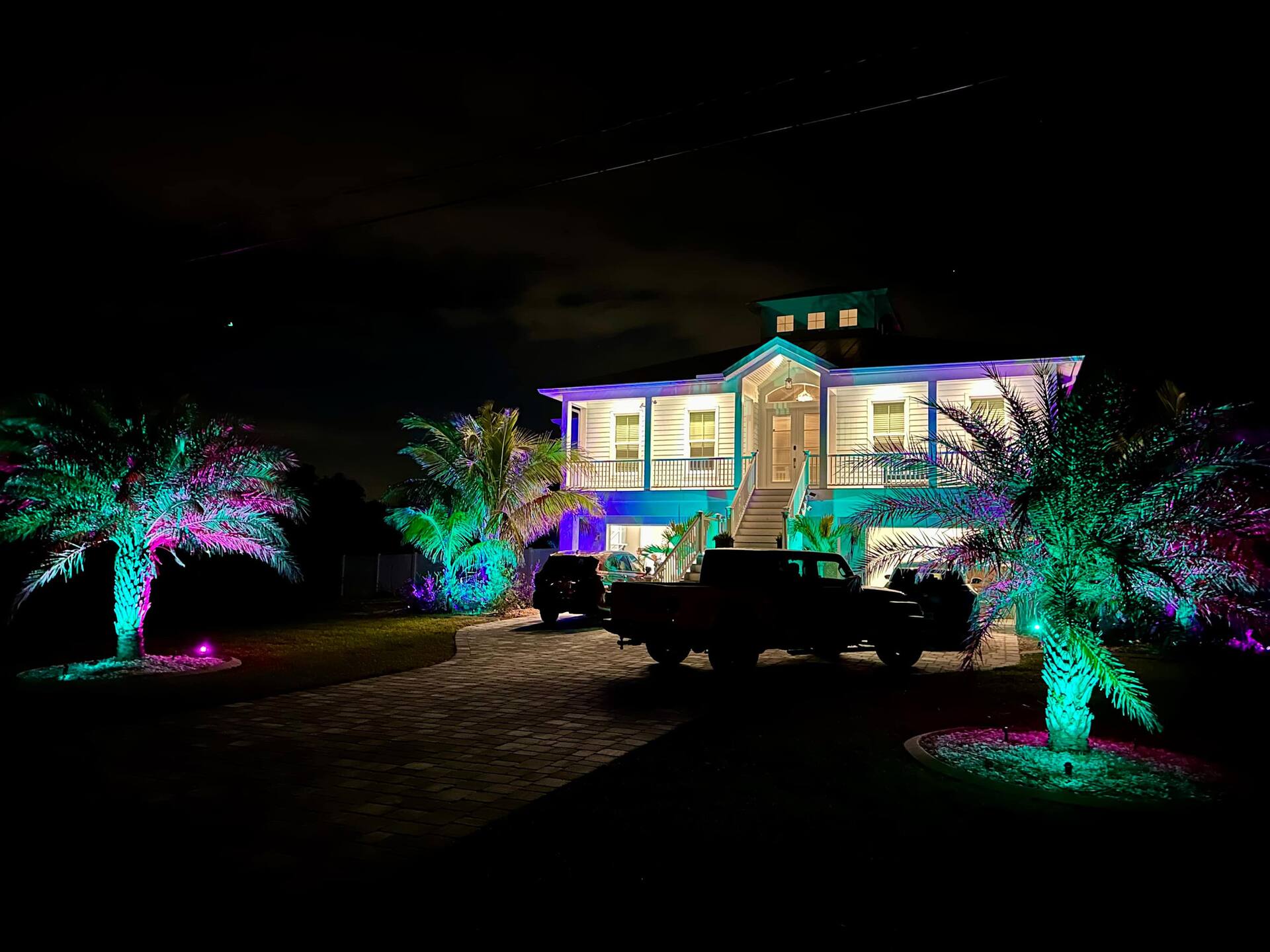 Home exterior lit with vibrant color lighting and palm trees at night