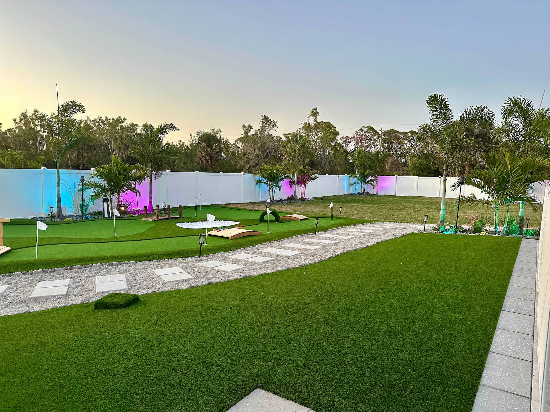 The private mini golf course in the Seaside Boca backyard at dusk — flagged greens, palms, and a lit path