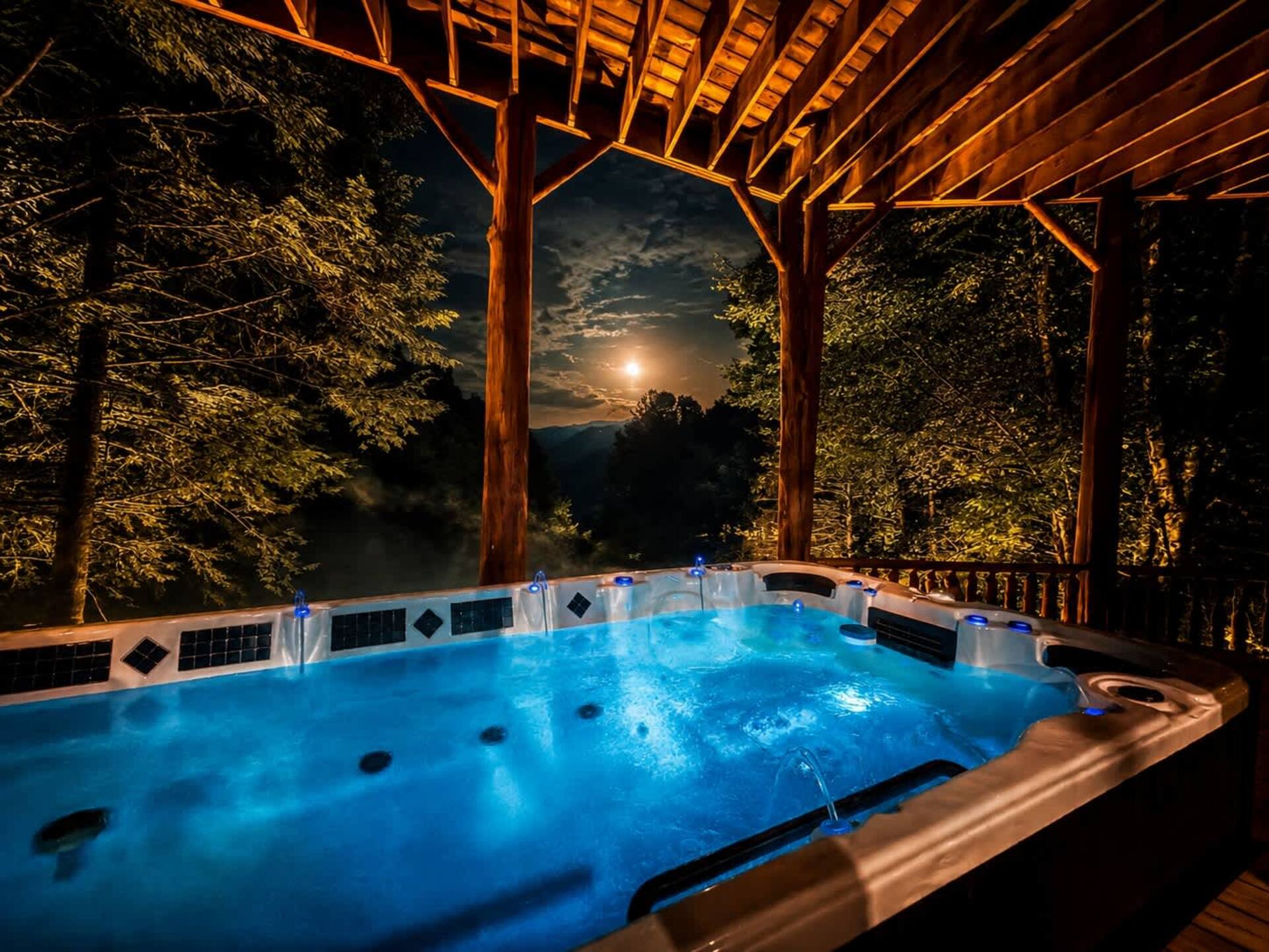 Swim spa lit up at night under the covered deck, with a moonlit view of the Smoky Mountains